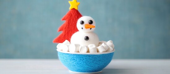 Snowman marshmallows in a bowl with red felt Christmas tree on white table festive winter holiday decoration concept.