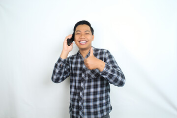 happy asian man showing thumb up while talking on mobile phone wearing plaid shirt isolated on white