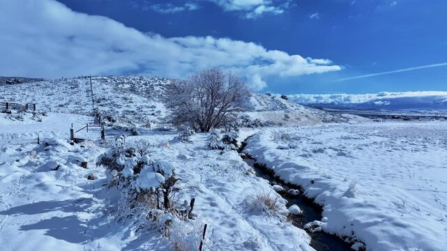 Aerial winter snow farm creek tree mountain. Storm and blizzard drops over a foot of fresh white snow. Rural farm community. Ranch farm, buildings, barns. Seasonal weather on livestock and wildlife.