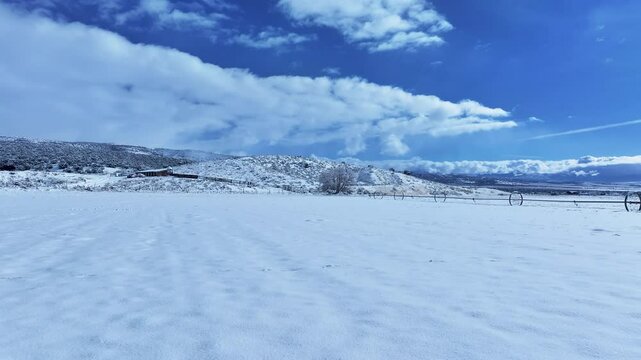 Aerial winter snow farm field valley Utah. Storm and blizzard drops over a foot of fresh white snow. Rural farm community. Ranch farm, buildings, barns. Seasonal weather on livestock and wildlife.
