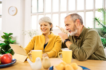 Senior couple using digital tablet at home having breakfast
