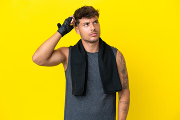 Young sport caucasian man with towel isolated on yellow background having doubts and with confuse face expression