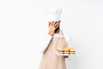 Young man holding muffin cake over isolated white background with tired and sick expression
