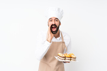 Young man holding muffin cake over isolated white background shouting and announcing something