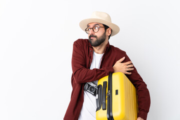 Traveler man man with beard holding a suitcase over isolated white background making doubts gesture...