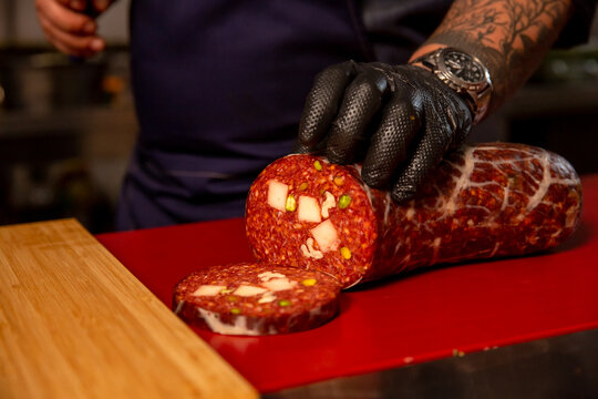Cook cuts pieces of homemade meat products. Slaughterhouse worker slicing handmade sausage in a butchers kitchen. - Powered by Adobe