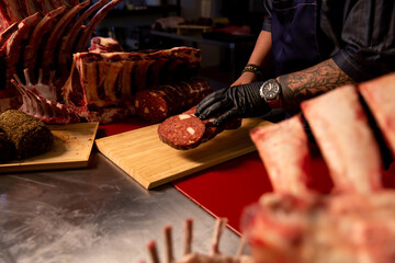 Slaughterhouse worker displaying freshly cut sausage slices in a butcher shop. Cook cuts pieces of homemade meat products. Cook cuts pieces of homemade meat products.