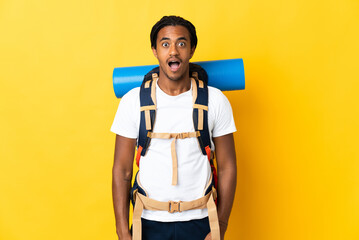 Young mountaineer man with braids with a big backpack isolated on yellow background with surprise facial expression