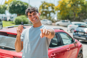 Young hispanic with car keys points finger at you with a confident expression