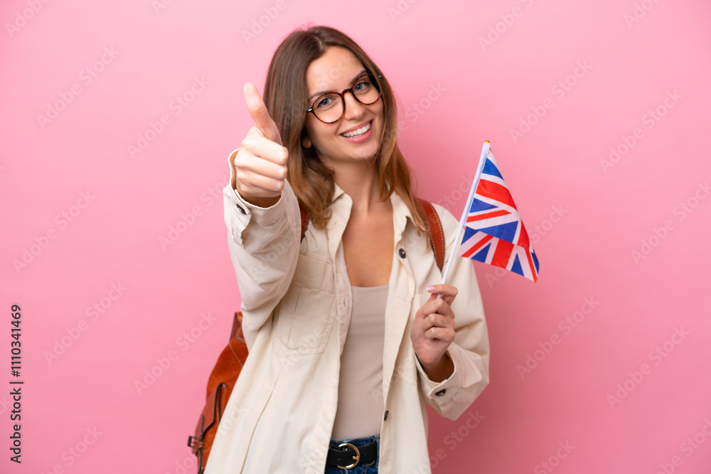 Wall mural Young student caucasian woman holding an United Kingdom flag isolated on pink background with thumbs up because something good has happened