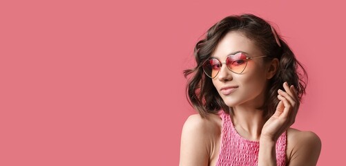 Pretty young woman wearing heart-shaped glasses on pink background with space for text. Valentine's Day celebration