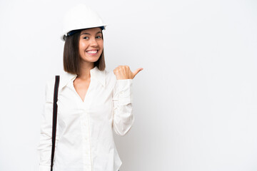 Young architect woman with helmet and holding blueprints isolated on white background pointing to the side to present a product