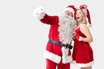 Santa Claus and beautiful woman taking selfie on white background