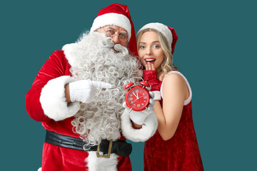 Santa Claus with beautiful woman pointing at alarm clock on green background