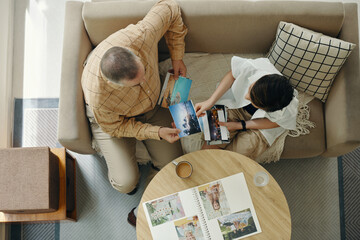 Top view of granddad and grandchild watching family photos together while sitting on sofa in the...