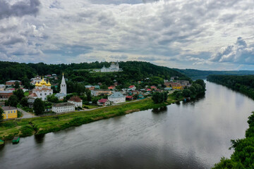 A picturesque landscape showcasing the Klyazma River as it flows through Gorokhovets, framed by lush greenery.