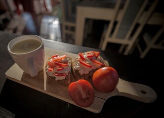 A wooden serving board with open-faced sandwiches topped with cottage cheese and tomato slices, served with fresh tomatoes and a cup of creamy coffee.