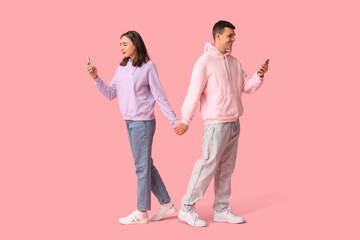 Young couple with mobile phones holding hands on pink background. Online dating