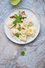 Ravioli served with different cheese and fresh basil, top view on a beige and blue stone background, vertical shot with space
