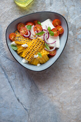 Grilled corn, feta cheese and cherry tomato salad, flat lay on a beige and blue stone background, vertical shot, copy space