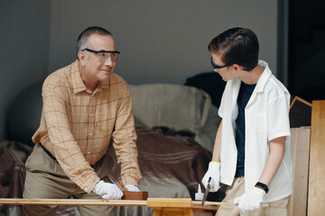 Grandfather teaching his son to saw the wood in the workshop