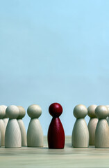 A single red figurine stands prominently among wooden peers, symbolizing individuality and the courage to be different in a sea of conformity.