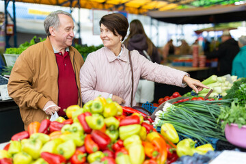 Happy mature male and female picking fresh organic vegetables during shopping at local bazaar