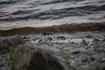 Soft waves create a rhythmic sound against the rocky shoreline, as the sun sets in the distance, painting the sky
