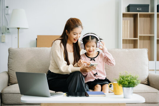 Cheerful mother and daughter sharing quality time on a couch, smiling and using a smartphone together.