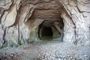 Dark cavern beckons explorers, showcasing rugged walls and a stony floor adorned with traces of past visitors.