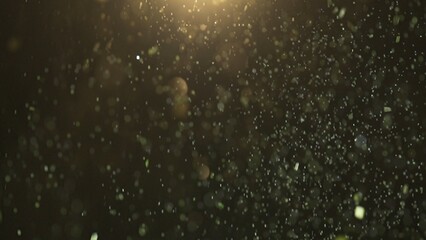 Many sparkling green glitters floating in light on black empty background with light from above.