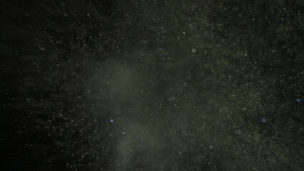 Many colorful sparkling glitters floating in light on empty black background with light from above.