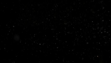 Many dust particles floating in light on empty black background with spotlight from above, close up view.