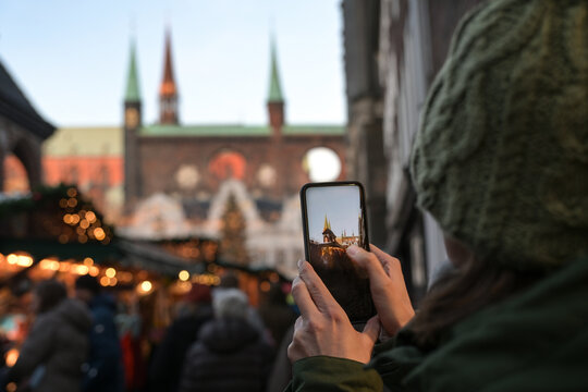 Woman from behind taking photos of the Christmas market with her smartphone in the historic old town of Lubeck in Germany, visible on the display, copy space, selected focus