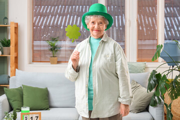 Senior woman in leprechaun hat holding paper clover at home