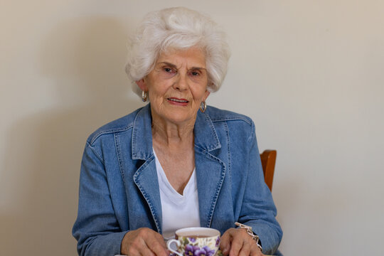 an elderly white-haired lady in her eighties sitting by herself with a cup of tea