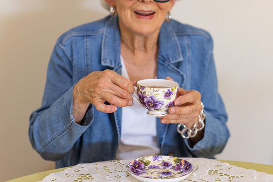 close image of elderly lady holding a cup of tea in a delicate floral china cup