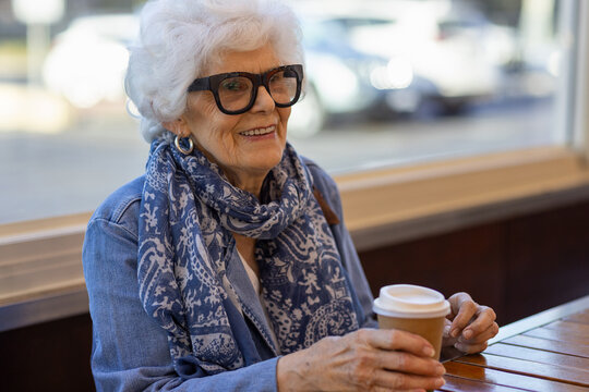 elderly lady sitting at cafe table with takeaway cup of coffee
