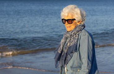 older lady wearing sunglass with scarf and denim jacket on the beach