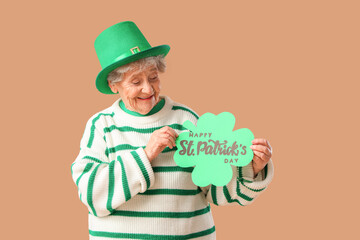Senior woman in leprechaun hat holding festive postcard with text HAPPY ST. PATRICK'S DAY on beige...