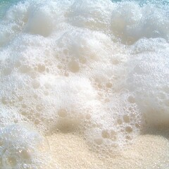 Obraz premium Close-up of white ocean foam on sandy beach.
