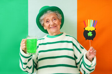 Happy senior woman in leprechaun hat with mug of green beer and decor for St. Patrick's Day...