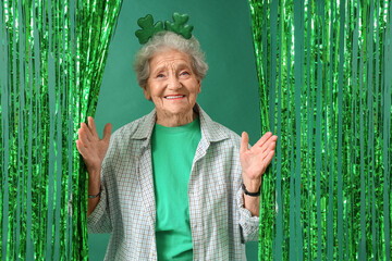 Happy senior woman with accessory for St. Patrick's Day celebration on green tinsel background