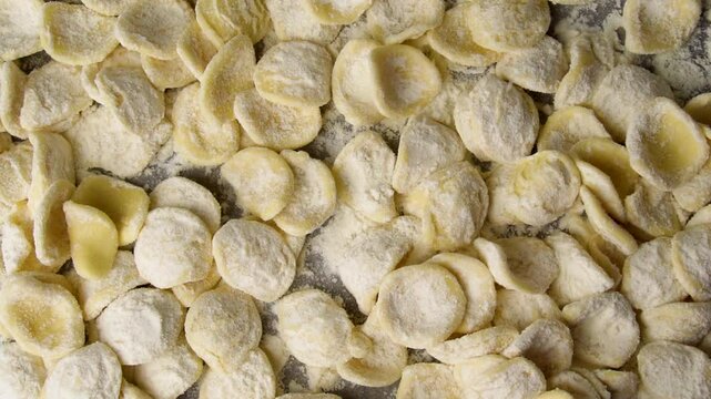 The traditional pasta type "orecchiette", tipical of Puglia, in Italy, have been coated in flour and are falling on a first layer of orecchiette. Closeup slow motion shot.