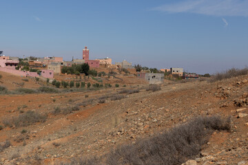A peaceful village in southern Morocco, with a mix of mudbrick and cement houses. The Atlas Mountains rise in the distance,