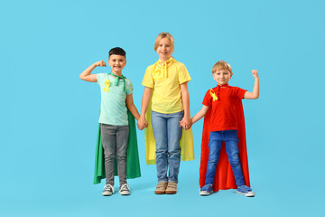 Fototapeta premium Little children dressed as superheroes with gold ribbons holding hands on blue background. Childhood cancer awareness concept