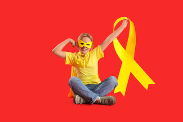 Little girl dressed as superhero with gold ribbon showing muscles on red background. Childhood cancer awareness concept