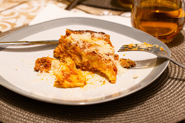 A slice of homemade lasagna, partially eaten, with gooey cheese on top, served on a gray plate. Perfect for food lovers and comfort meal enthusiasts.