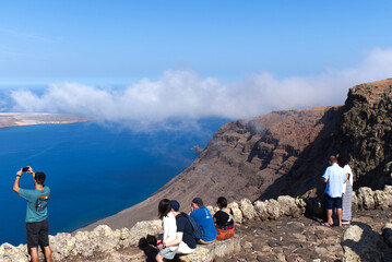 Tourists enjoying the viewpoint from Mirador Del Rio on Lanzarote of La Graciosa Island in the Canary Islands and the dramatic cliffs.