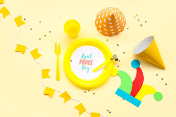 Table setting with festive postcard, confetti and party decor for April Fools Day on yellow background